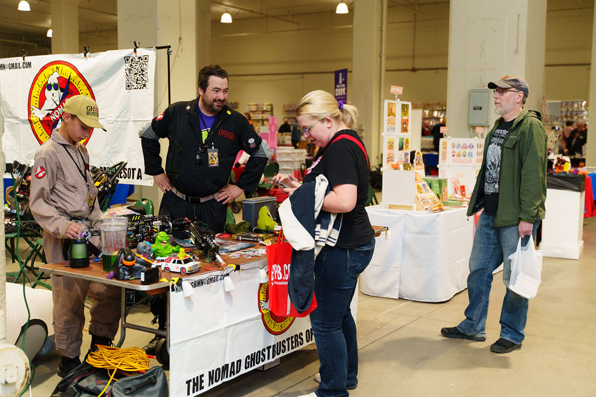 two people holding yellow plastic bags full of comic books and handing them out to attendees at admissions